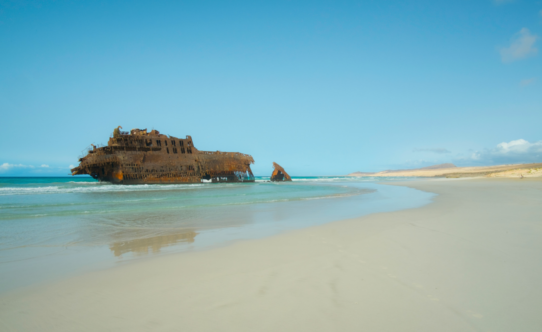 Naufrágio do navio Cabo Santa Maria encalhado na praia da Ilha da Boavista, em Cabo Verde, com areia clara, mar calmo e céu azul num cenário icónico e isolado do arquipélago.