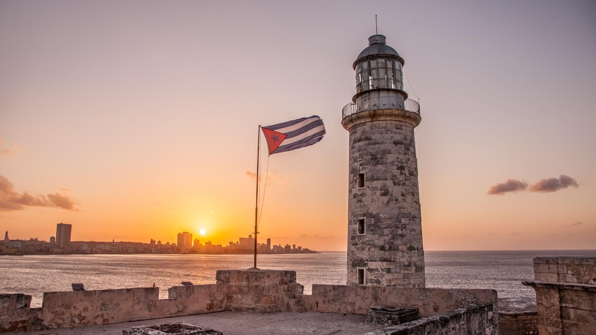 Vista do farol do Castillo del Morro com a bandeira de Cuba ao vento durante o pôr do sol sobre o horizonte de Havana.