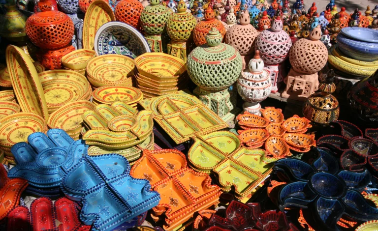 Peças de cerâmica artesanal colorida expostas num mercado de Djerba, Tunísia, incluindo travessas, pratos e objetos decorativos com padrões tradicionais tunisinos.
