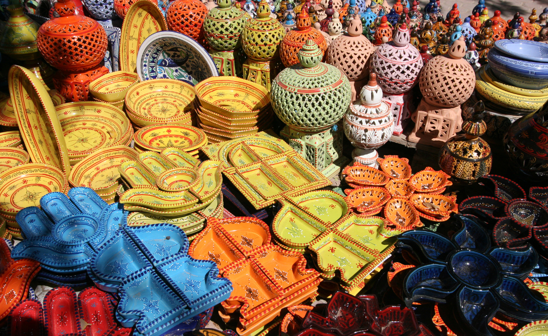 Peças de cerâmica artesanal colorida expostas num mercado de Djerba, Tunísia, incluindo travessas, pratos e objetos decorativos com padrões tradicionais tunisinos.