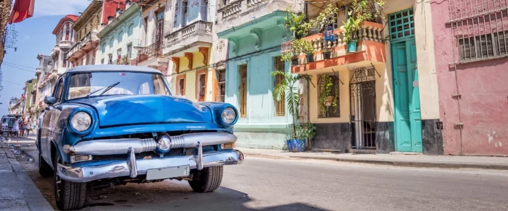 Carro clássico azul estacionado numa rua típica de Havana, Cuba, com fachadas coloniais coloridas ao fundo.