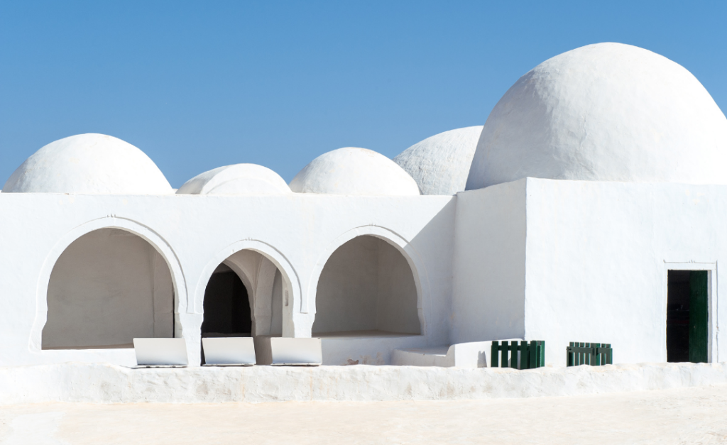 Edifício tradicional de Djerba com cúpulas brancas e arcos, destacado contra um céu azul claro típica da arquitetura tunisina.