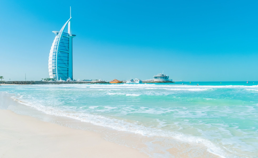 Praia de areia branca em Dubai com águas turquesa e vista clara para o icónico hotel Burj Al Arab junto ao mar.