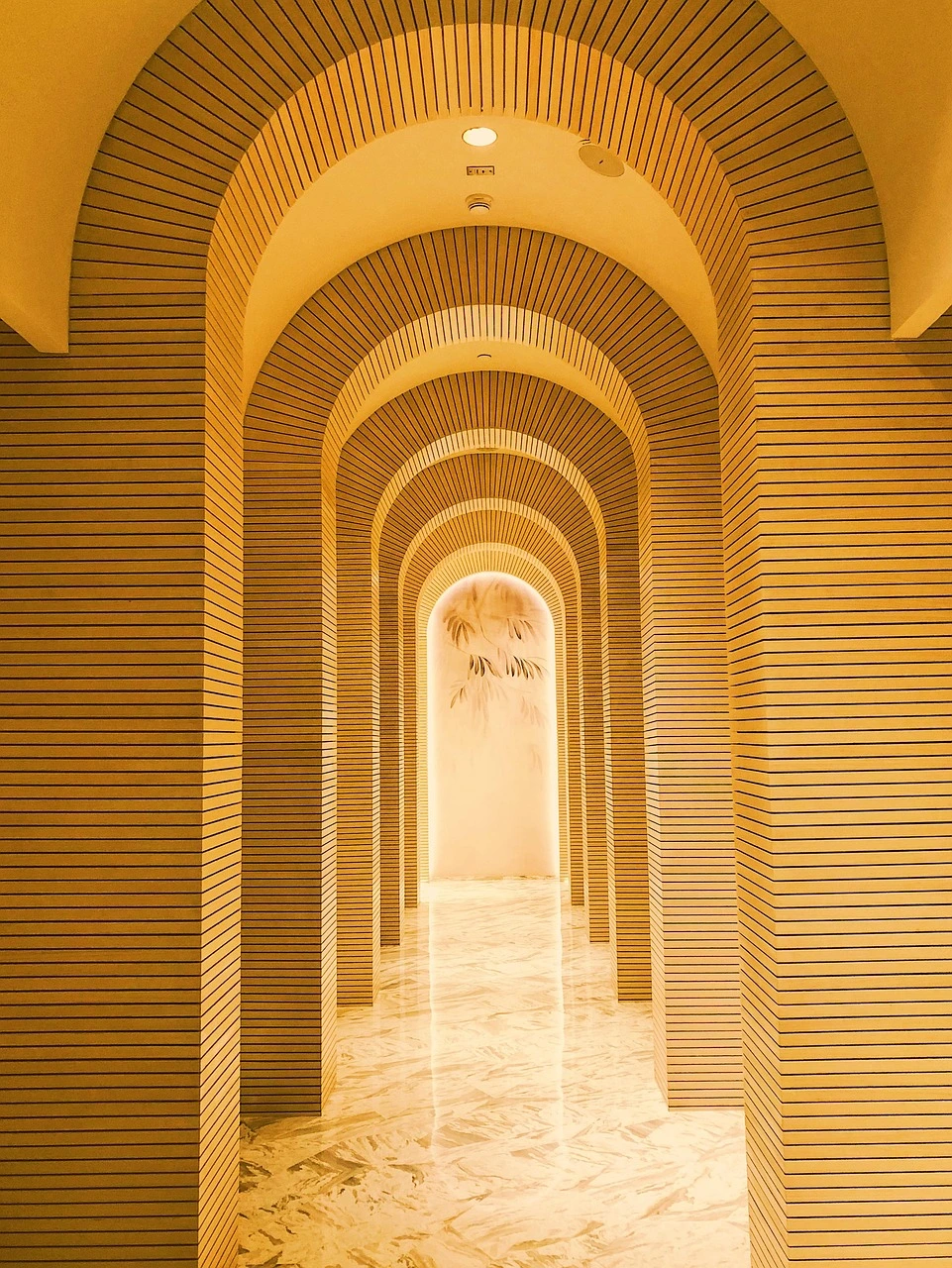 Corredor elegante com arcos repetidos e iluminação dourada, criando um efeito visual moderno inspirado na arquitetura árabe.