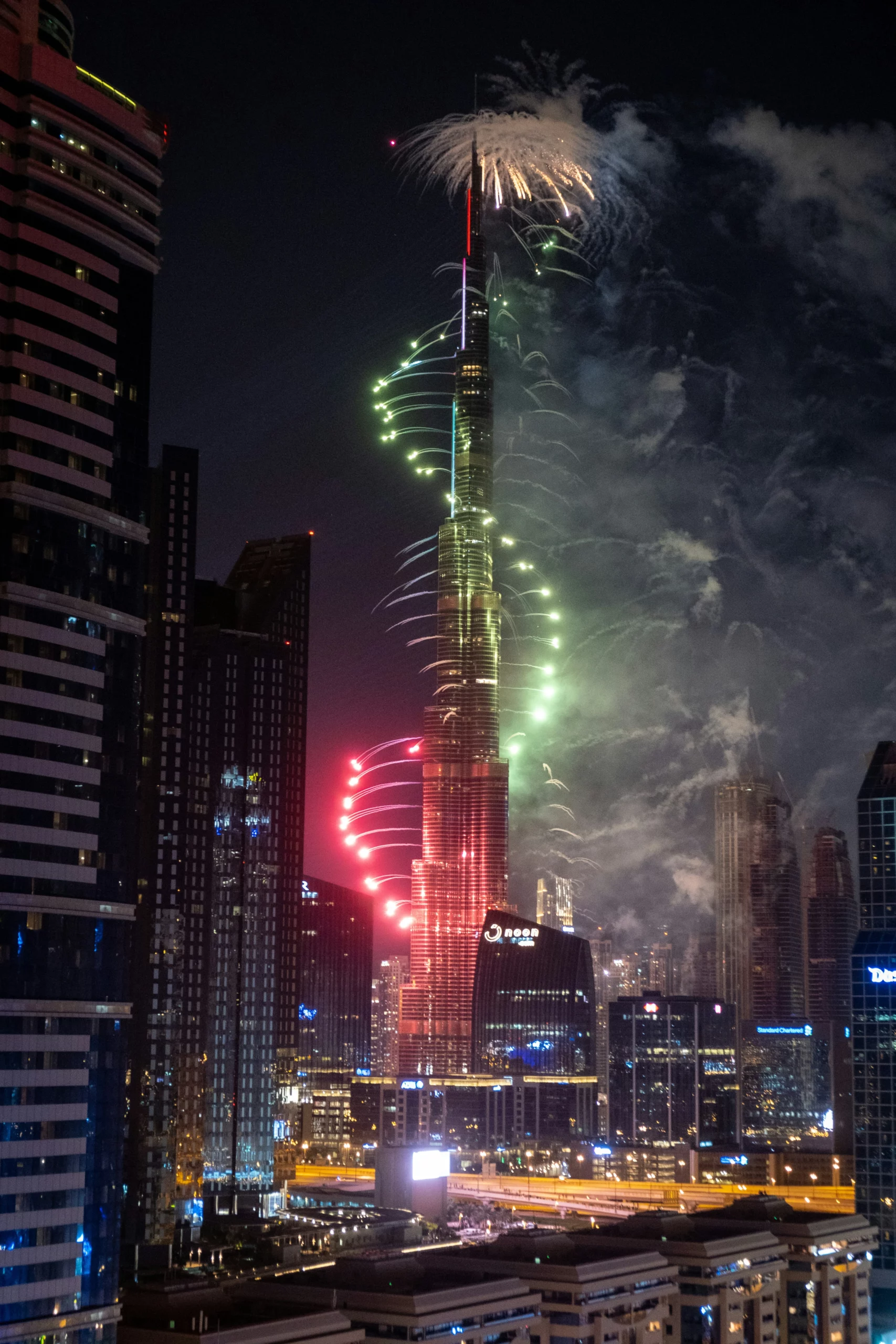 Burj Khalifa iluminado à noite com fogo-de-artifício colorido a subir pela torre, rodeado pelos arranha-céus de Downtown Dubai.