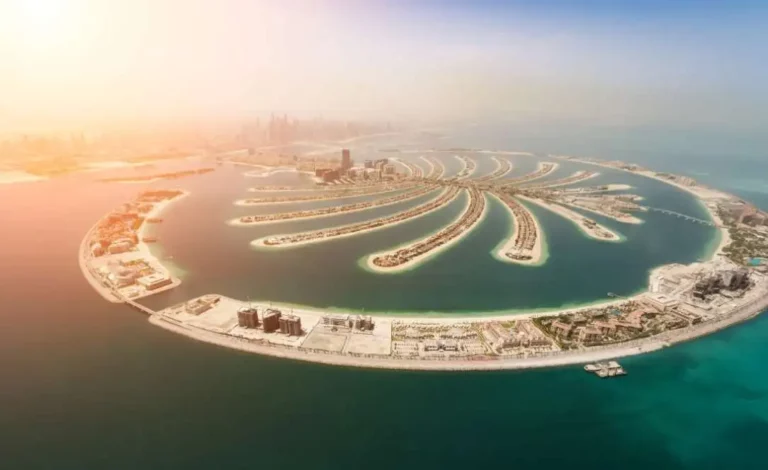 Vista aérea da Palm Jumeirah no Dubai, mostrando o formato de palmeira com as suas frondes, rodeada por águas azul-turquesa e com o horizonte urbano ao fundo.