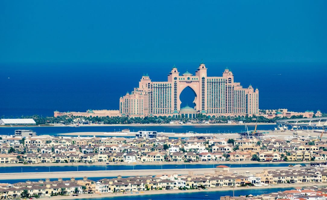 Vista frontal do hotel Atlantis The Palm em Dubai, com o oceano azul ao fundo e moradias da Palm Jumeirah espalhadas à frente.