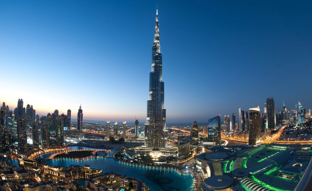 Vista panorâmica de Downtown Dubai ao anoitecer, com o Burj Khalifa iluminado ao centro e o lago do Dubai Mall rodeado por arranha-céus modernos.