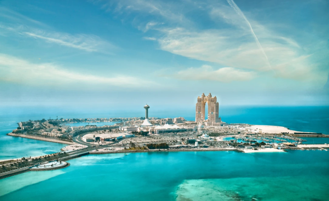 Vista aérea de Al Marina em Abu Dhabi, com águas azul-turquesa, a torre de observação Marina Eye e os Nation Towers ao fundo.
