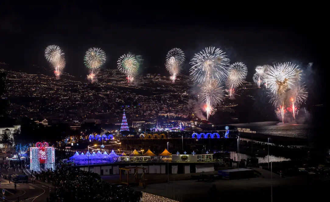 Vista noturna do Funchal iluminado pelo famoso fogo-de-artifício de fim de ano, com o anfiteatro da cidade e o porto da Madeira brilhando sob as luzes festivas.