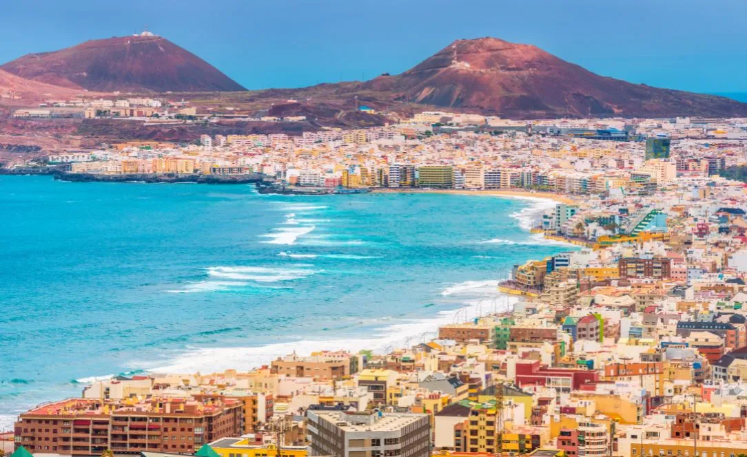 Vista panorâmica de Las Palmas de Gran Canaria, com a Praia de Las Canteras, mar azul intenso e montanhas vulcânicas ao fundo.