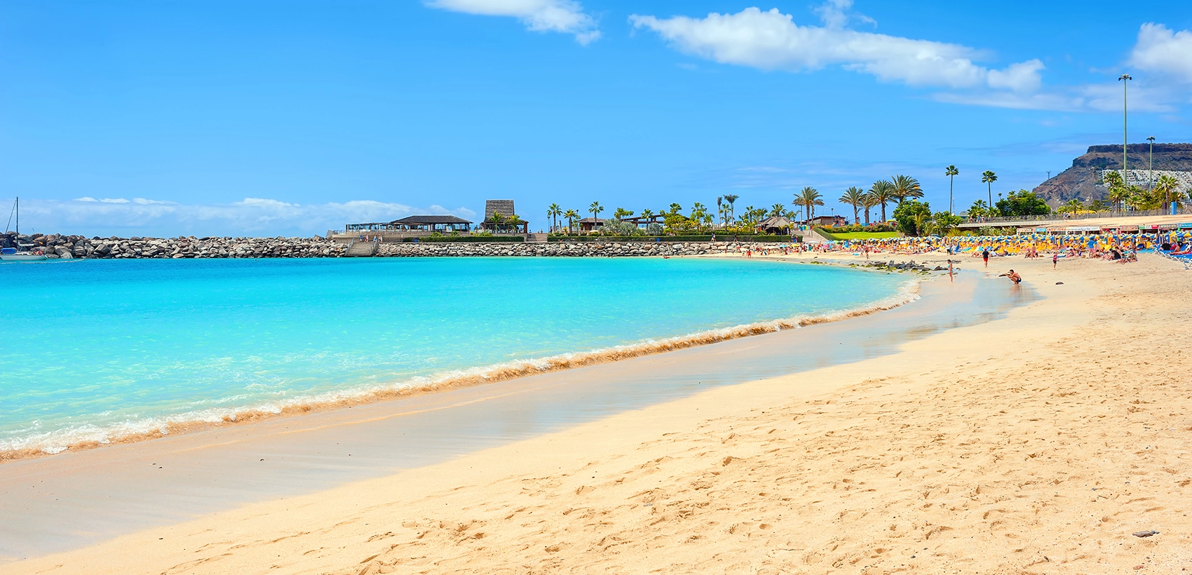 Praia de Amadores, em Gran Canaria, com água turquesa cristalina, areia dourada e zona de banhistas sob um céu azul limpo.