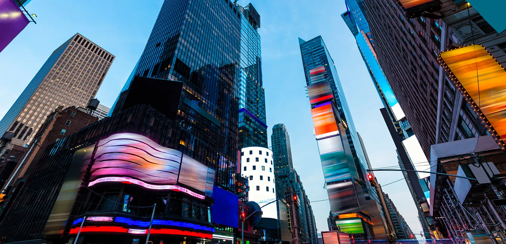Vista de Times Square ao entardecer, com arranha-céus iluminados, painéis publicitários coloridos e ruas movimentadas.