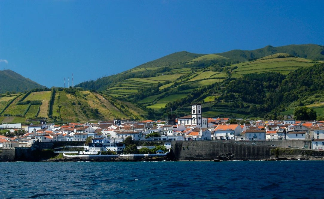 Vista costeira da Ribeira Grande, em São Miguel, Açores, com as casas de telhados laranja, a igreja matriz e as encostas verdes em socalcos ao fundo.