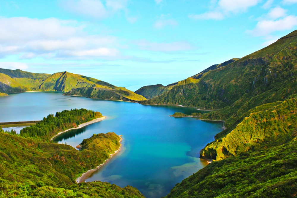 Vista panorâmica da Lagoa do Fogo, em São Miguel, Açores, com água azul-turquesa rodeada por montanhas verdes e vegetação natural.