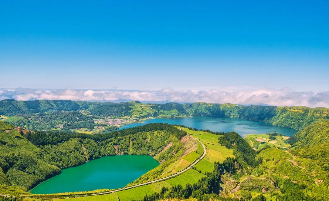 Paisagem panorâmica das Lagoas das Sete Cidades, mostrando a Lagoa Verde e a Lagoa Azul rodeadas por montanhas verdes sob céu azul limpo.
