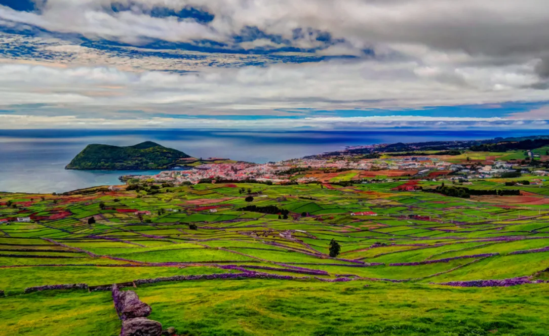 Paisagem panorâmica da Ilha Terceira, mostrando os campos verdes, a cidade de Angra do Heroísmo e o Monte Brasil projetado sobre o oceano Atlântico.
