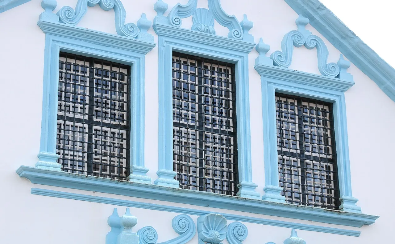 Fachada branca com detalhes azul-claro e três janelas tradicionais gradeadas, típica da arquitetura histórica da Ilha Terceira, Açores.