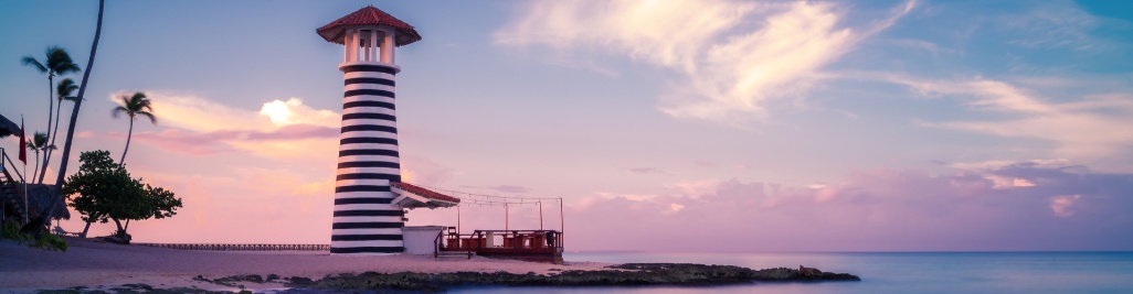Farol icónico de Bayahibe junto ao mar, ao pôr do sol, com céu rosado e águas calmas do Caribe.